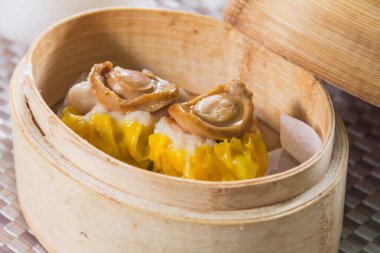 Üzerinde küçük deniz kulağı parçaları olan iki siu mai hamur tatlısı olan bambu budan bir buhar tenceresi..