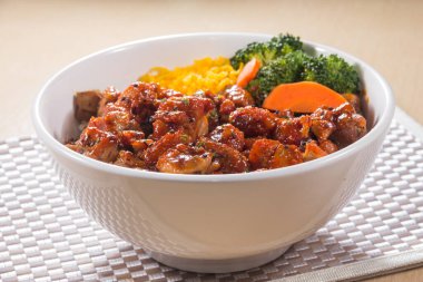 Teriyaki soslu pilav, brokoli, havuç ve doğranmış yumurta ile dolu beyaz bir kase..