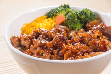 Teriyaki soslu pilav, brokoli, havuç ve doğranmış yumurta ile dolu beyaz bir kase..