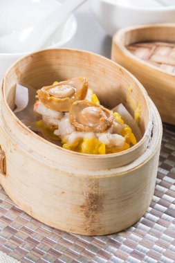 Üzerinde küçük deniz kulağı parçaları olan iki siu mai hamur tatlısı olan bambu budan bir buhar tenceresi..