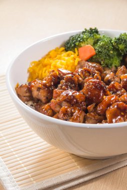 Teriyaki soslu pilav, brokoli, havuç ve doğranmış yumurta ile dolu beyaz bir kase..