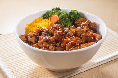 Teriyaki soslu pilav, brokoli, havuç ve doğranmış yumurta ile dolu beyaz bir kase..