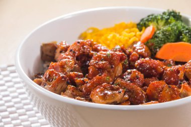 Teriyaki soslu pilav, brokoli, havuç ve doğranmış yumurta ile dolu beyaz bir kase..