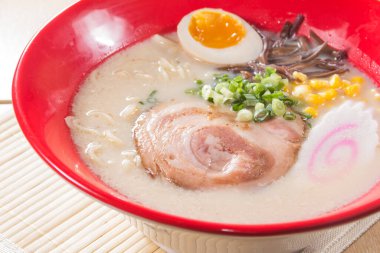 Kırmızı bir kase kremalı ramen çorbası dilimlenmiş domuz eti, yarı haşlanmış yumurta, mısır ve yeşil soğanlı garnitür..