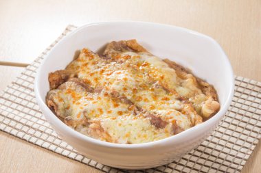 Erimiş altın peynirle kaplı pirinç ve sığır eti dilimleriyle dolu beyaz bir seramik tabak..