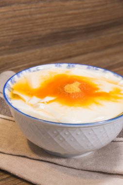 Beyaz bir seramik kase, bej bir bezin üzerine yerleştirilmiş altın şurup ve şeker tozuyla kaplı pürüzsüz fasulye kaymağı ile dolu..