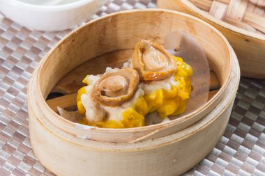 Üzerinde küçük deniz kulağı parçaları olan iki siu mai hamur tatlısı olan bambu budan bir buhar tenceresi..