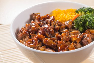 Teriyaki soslu pilav, brokoli, havuç ve doğranmış yumurta ile dolu beyaz bir kase..