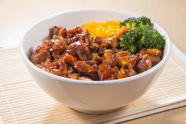 Teriyaki soslu pilav, brokoli, havuç ve doğranmış yumurta ile dolu beyaz bir kase..