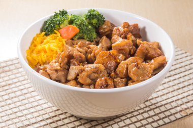 Teriyaki soslu pilav, brokoli, havuç ve doğranmış yumurta ile dolu beyaz bir kase..