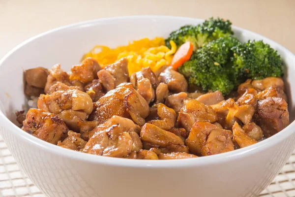 Teriyaki soslu pilav, brokoli, havuç ve doğranmış yumurta ile dolu beyaz bir kase..