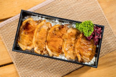 Pirinç ve garnitürle servis edilen ızgara domuz dilimli dikdörtgen bento kutusu..