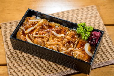 Siyah bento kutusunda servis edilen soğanlı ızgara domuz dilimleri..