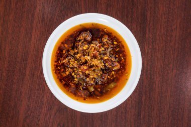 Ahşap bir masanın üzerinde kırmızı biber ve baharatla dolu kırmızı biber dolu beyaz bir kase..