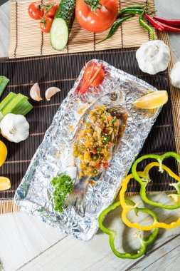 Limon dilimli folyoyla servis edilen kırmızı biberli ve otlu ızgara balığın yakın çekimi..