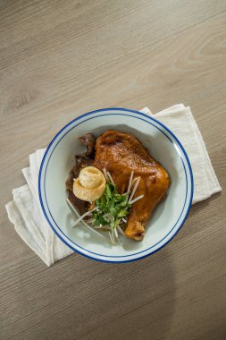 Üstünde taze otlar ve sebzelerle servis edilen haşlanmış tavuk budu olan beyaz bir kase..