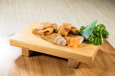 Ahşap tahta, terbiye edilmiş mürekkep balığı dilimleri yeşil garnitürle düzgünce dizilmiş..