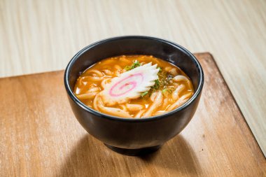 Pembe kıvrımlı balık kekiyle kaplı miso çorbasında kalın udon şehriyeleriyle dolu siyah bir kase..