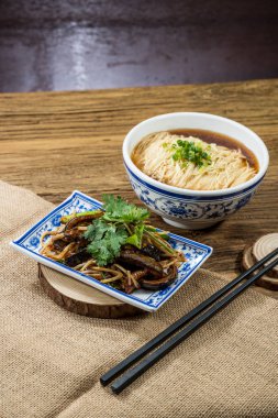 Soya bazlı çorbada ince erişteyle dolu mavi desenli bir kase kişniş ve yeşil soğanla süslenmiş bir tabak haşlanmış yılan balığı..