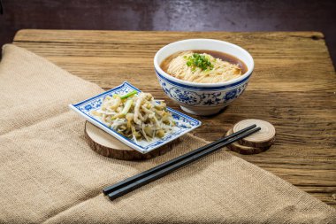 Soya bazlı çorbada ince erişteyle dolu mavi desenli bir kase kişniş ve yeşil soğanla süslenmiş bir tabak haşlanmış yılan balığı..