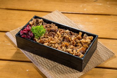 Pirinçle servis edilen, maydanoz ve sebze turşusuyla süslenmiş, haşlanmış sığır dilimleriyle dolu dikdörtgen bir bento kutusu..