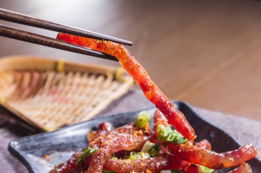 Yakın plan bir yemek çubuğu. Baharatlı domuz kulağı şeridini doğranmış yeşil soğanla süslenmiş siyah bir tabağın üzerinde tutuyorlar..