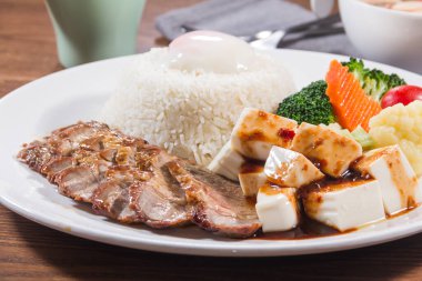 Teriyaki bifteği dilimlenmiş buğulanmış pirinç soslu tofu küpleri ve brokoli ve havuç da dahil olmak üzere çeşitli sebzeler..