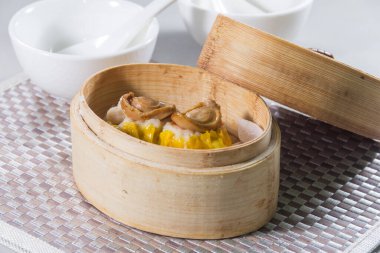 Üzerinde küçük deniz kulağı parçaları olan iki siu mai hamur tatlısı olan bambu budan bir buhar tenceresi..