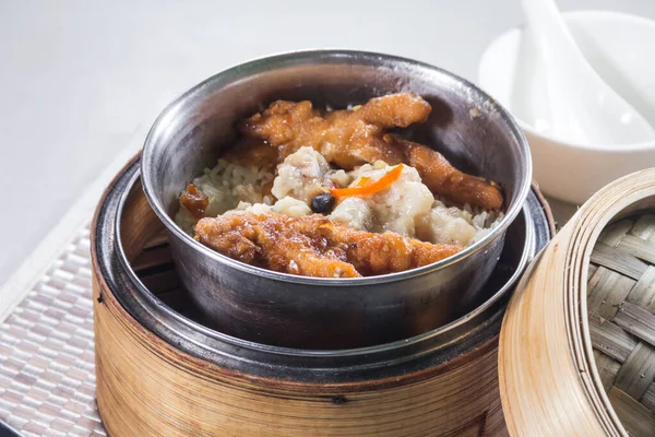 Siyah fasulye soslu buğulanmış metal bir kase domuz pirzolası bambu buharı sepetinde pilav ile servis edilir..