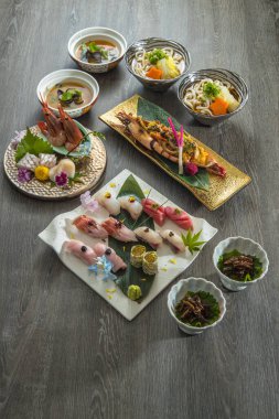 Japon yemek takımının üstten görünüşü udon kaseleri, miso stili çorbalar, çeşitli nigiri 'ler, ve bir kaplama karides. Temiz düzenleme ve doğal sofra takımı sunumda tazeliği ve uyumu vurguluyor.