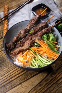 İnce dilimlenmiş çiğ balık ön planda yapraklarla süslenmiş bir şekilde duruyor. Arkasında yeşil, mantar, tofu ve kök sebzeleri küçük daldırma kapları olan bambu bir hasırın üzerinde saklar..