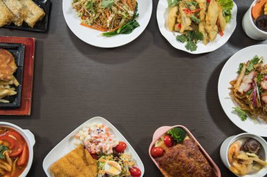 Pişmiş yemeklerden oluşan bir seçim karanlık bir masanın kenarlarını çerçeveler ve ortada cömert bir kopya alanı bırakır. Erişte, salata, haşlanmış et ve çorbalar menüler veya tanıtım planları için uygun renkli bir genel görünüm oluşturur.