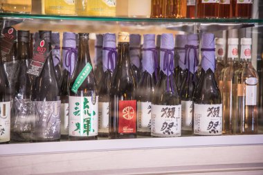 Mor kablolar ve kağıt etiketlerle bağlanmış kaliteli sake şişeleriyle dolu bir dolaba yakından bakmak. Cam ve düzenli sıralardaki yansımalar ince bir tat alma ve perakende atmosfer sağlar..