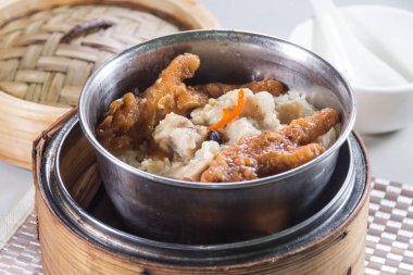 Siyah fasulye soslu buğulanmış metal bir kase domuz pirzolası bambu buharı sepetinde pilav ile servis edilir..