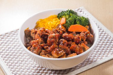 Kızarmış teriyaki dolu beyaz bir kase. Tavuk parçaları. Brokoli ve havuçla servis ediliyor..