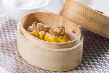 Üzerinde deniz kulağı olan iki parça sarı siu mai örülmüş bir hasırın üzerindeki bambu budan bir buharlı vapurda servis edilir.