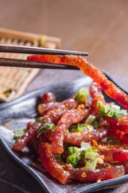 Bir tabak taze soğanla süslenmiş baharatlı domuz eti şeridi tutan bir yemek çubuğu.