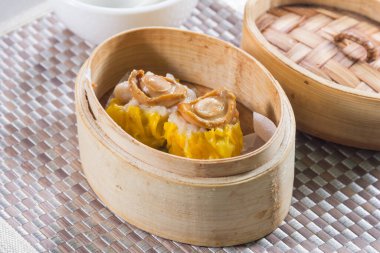 Bir bambu buharlı sepet, iki sarı siu mai hamur köftesi ve deniz kulağı parçaları..