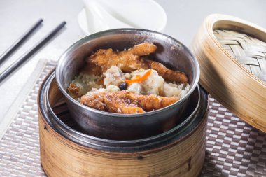 Küçük metal bir kase buharda pişmiş pirinç tavuk ayağı ve domuz kaburgası ile kaplanır ve bambu budan bir buharlı tencerenin içine yerleştirilir. Kompozisyon, buharlı gemiden sıcak servis edilen klasik bir Dim Sum öğesi yakalıyor..