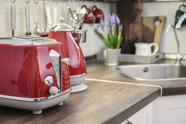 Red toaster and electric kettle in retro slile on tabletop in kitchen interior.