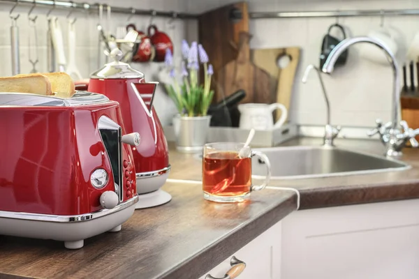 Red electric kettle and toaster  in retro slile with bread and cap of tea in kitchen interior closeup