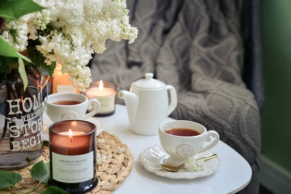 コーヒーテーブルの上のライラックの花の花束は 自宅のインテリアでお茶と燃えるキャンドルのカップ — ストック写真