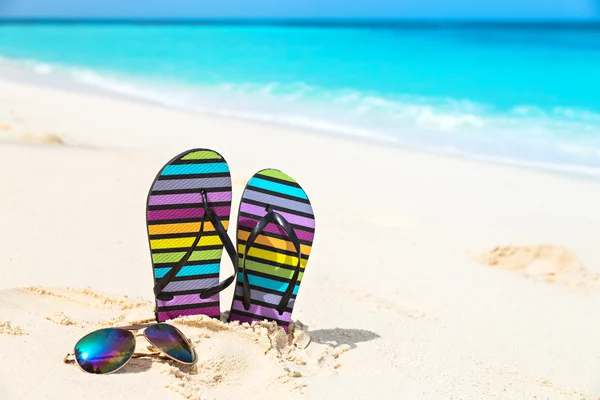 Chanclas multicolores y gafas de sol en una playa soleada — Foto de Stock