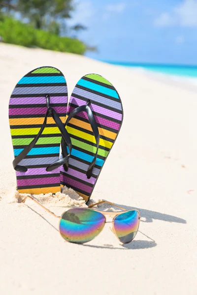 Multicolored flip-flops and sunglasses on a sunny beach — Stock Photo, Image