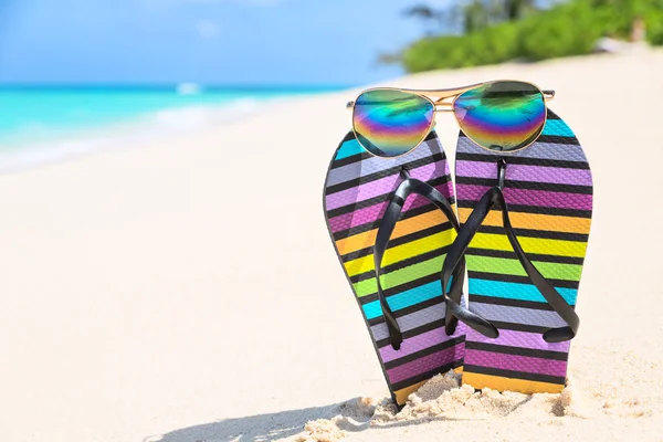 Multicolored flip-flops and sunglasses on a sunny beach — Stock Photo, Image