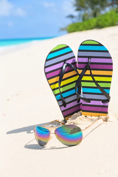 Chanclas multicolores y gafas de sol en una playa soleada — Foto de Stock