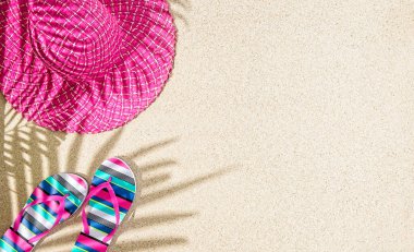 Büyük yuvarlak pembe yaz şapkası ve renkli çizgili sandaletler kum üzerinde palmiye ağacı gölgesi 
