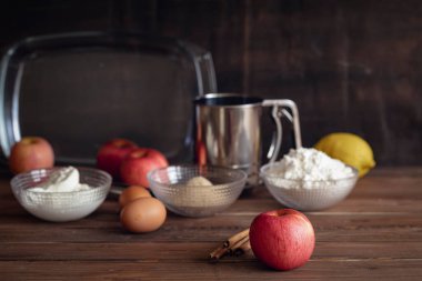 Tarçın çubuklu büyük kırmızı elma ve koyu kahverengi arka planda elmalı turta pişirmek için temel malzemeler. 