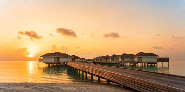 Muelle de madera y villas de agua en el tiempo de puesta del sol por la playa tropical — Foto de Stock