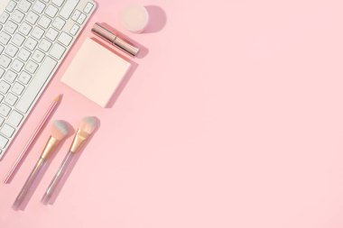 Pembe arka planda klavyesi ve kozmetik aksesuarları olan ofis kadınsı masası, kopyalama alanı olan düz masa
